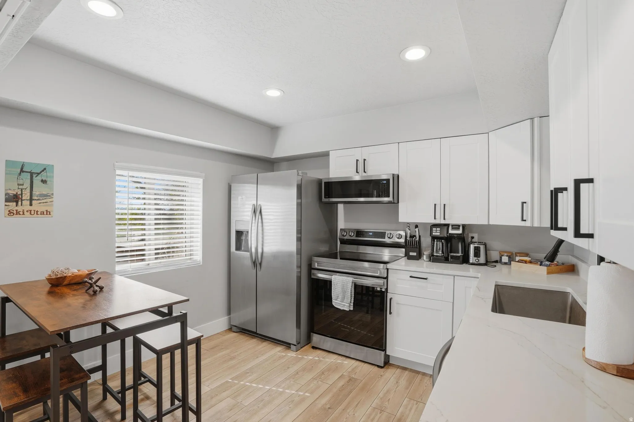 Furnished Unit #44 faces West. Kitchen with stainless steel appliances, white cabinets, light wood-style flooring, light stone countertops, and recessed lighting