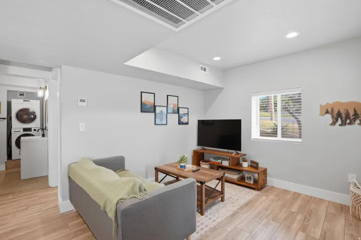 Furnished Unit #44 faces West. Living area with light wood-style flooring, stacked washer / drying machine, and recessed lighting