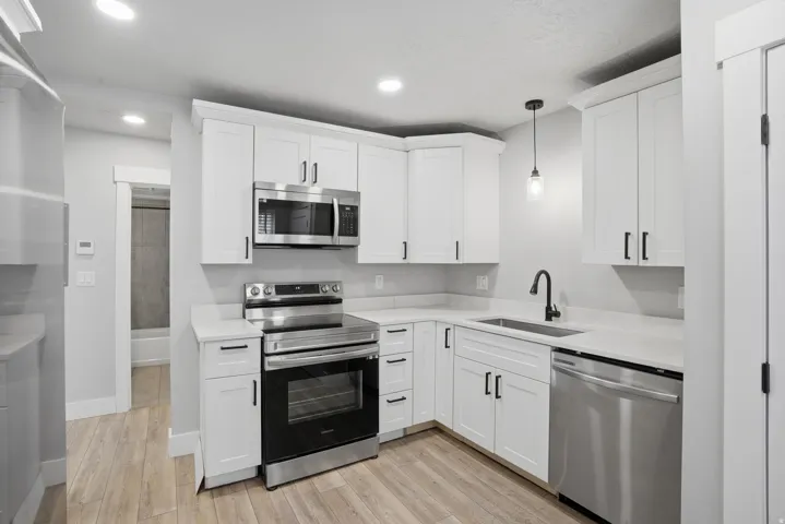 Unit #40 Kitchen with stainless steel appliances, decorative light fixtures, light wood-type flooring, and white cabinetry