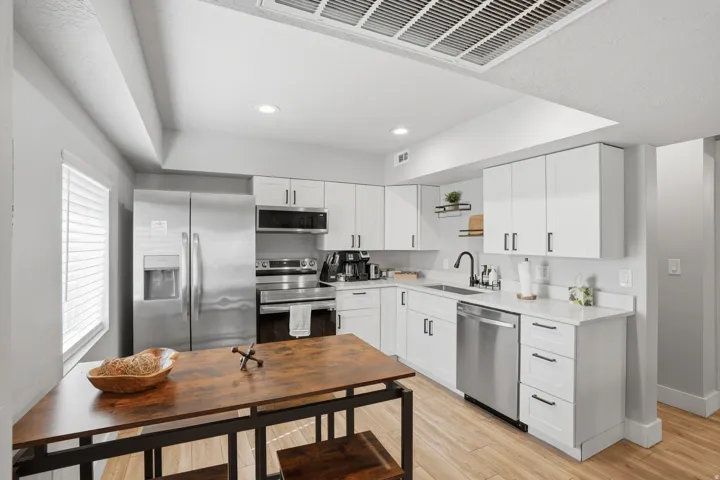 Furnished Unit #44 faces West. Kitchen with stainless steel appliances, white cabinetry, light wood-style floors, recessed lighting, and light stone counters