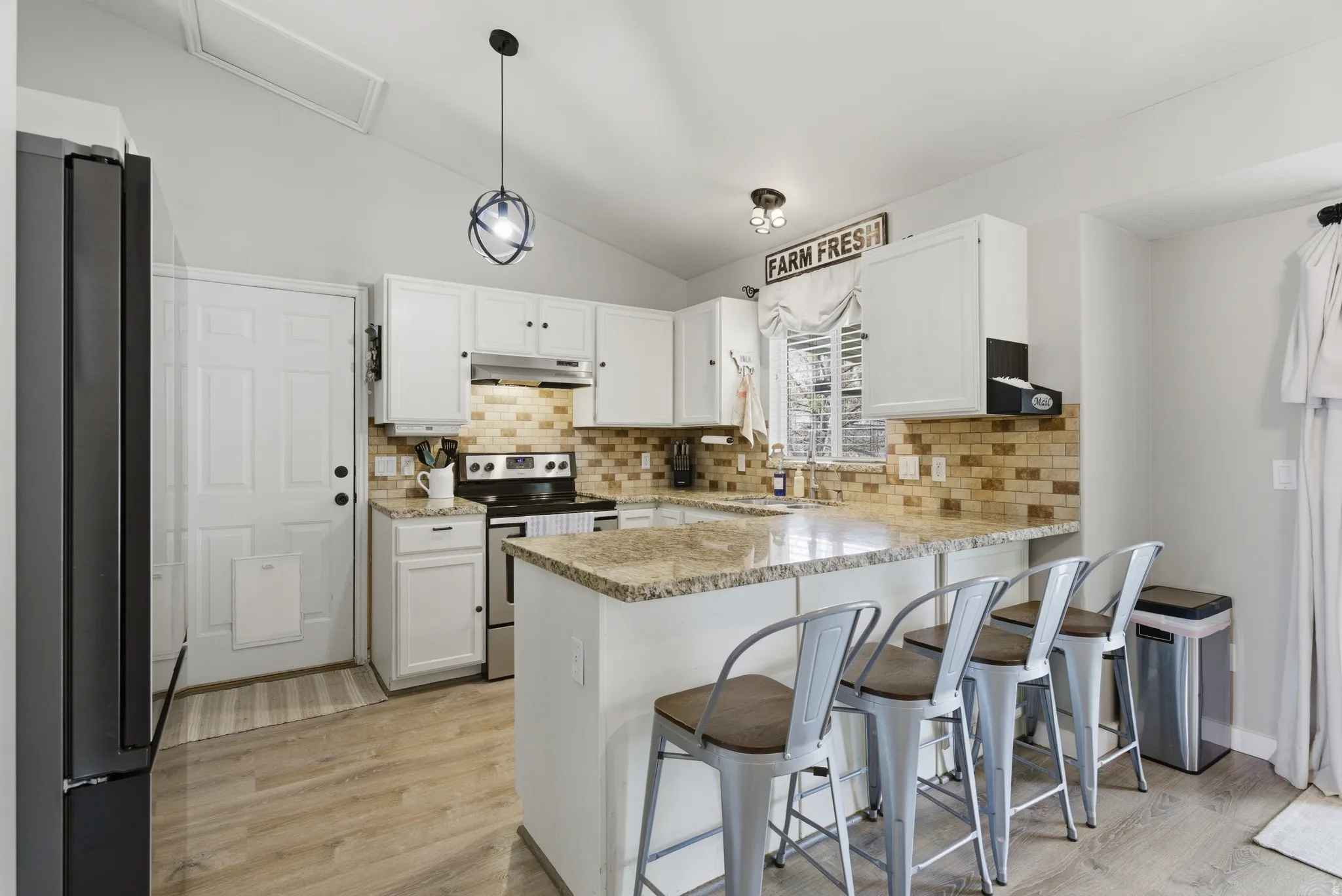 Kitchen with a breakfast bar area, freestanding refrigerator, vaulted ceiling, and white cabinetry