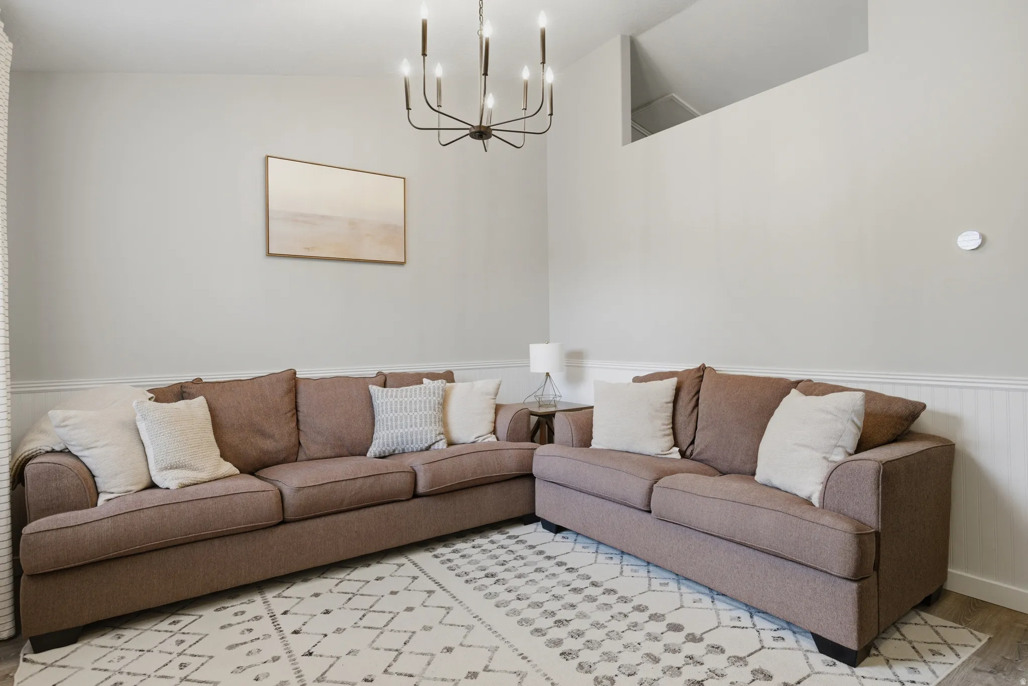 Living room featuring vaulted ceiling, a chandelier, light wood finished floors, and wainscoting