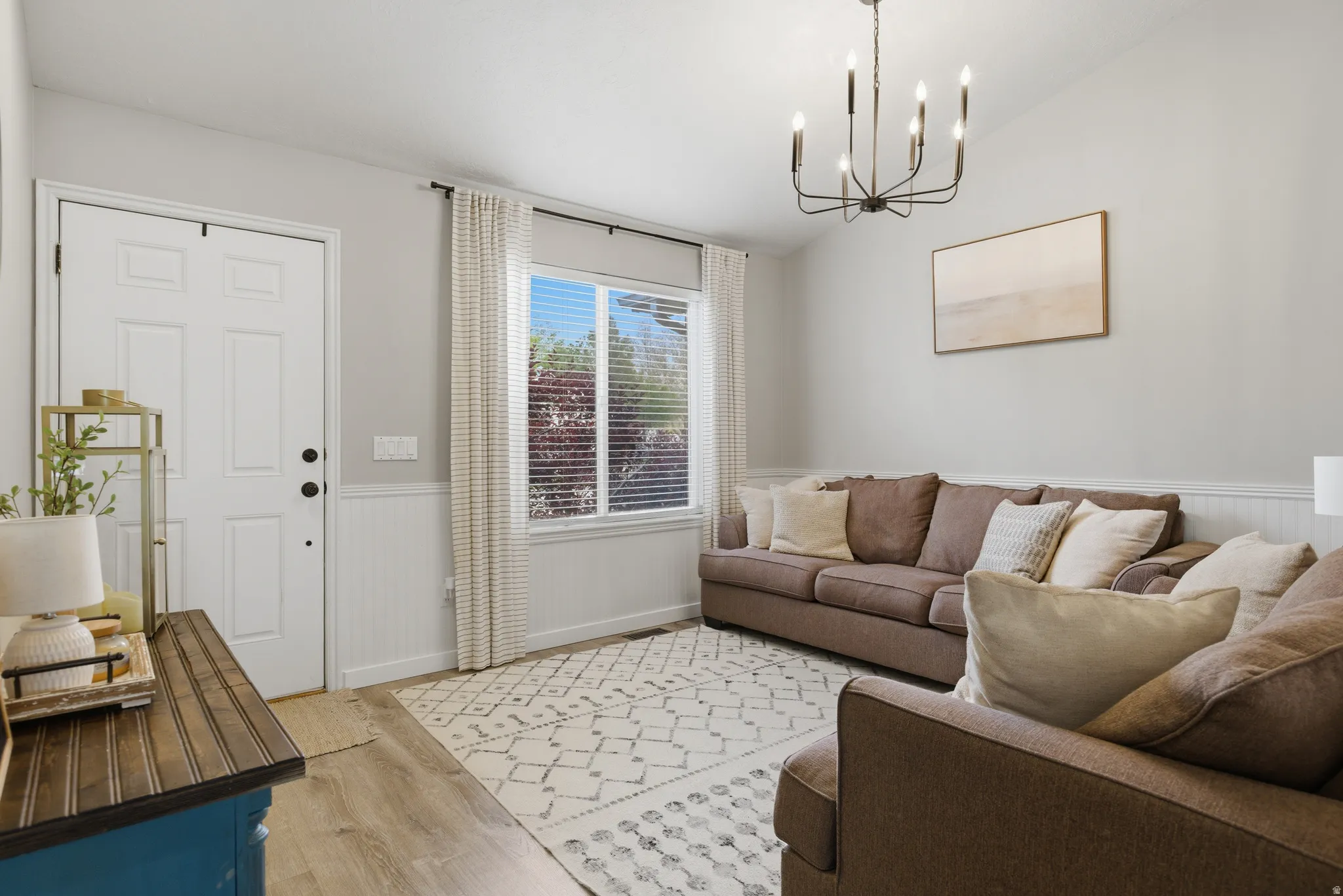 Living area with wainscoting, vaulted ceiling, light wood finished floors, and hanging lights