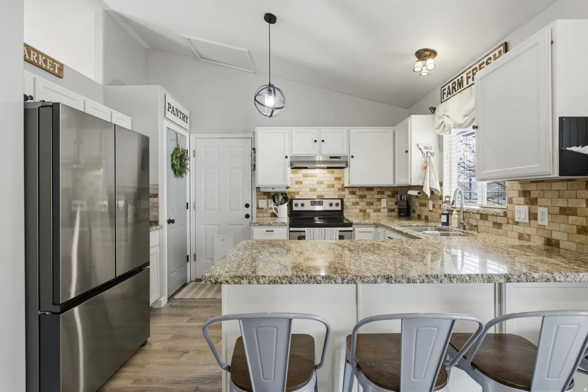 Kitchen featuring stainless steel appliances, a peninsula, light stone countertops, white cabinetry, and vaulted ceiling