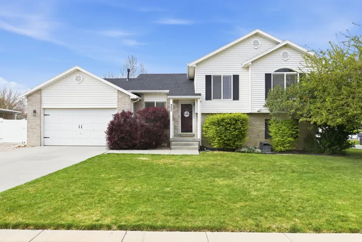 Split level home featuring brick siding, a front yard, a garage, concrete driveway, and roof with shingles