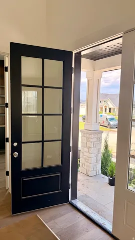 Entryway featuring a dark paneled door with multiple glass lites, wood-finish flooring, and a stone-clad porch pillar