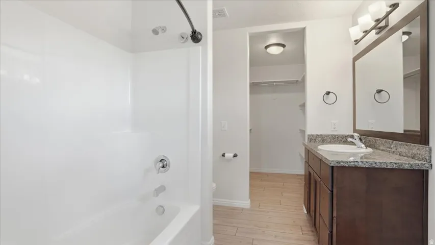 Bathroom featuring vanity, light wood-style floors, bathtub / shower combination, and a spacious closet