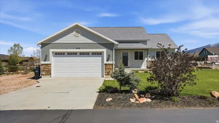 View of front of house with an attached garage, concrete driveway, stone siding, and a front lawn