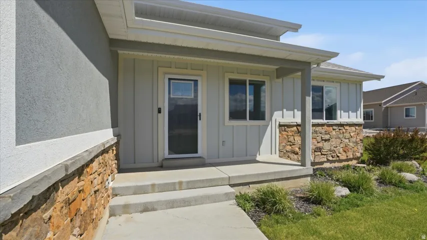 View of exterior entry with board and batten siding, covered porch, and stone siding