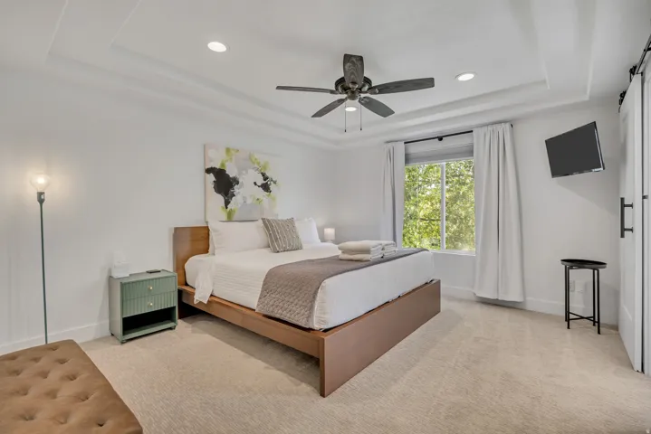 Bedroom featuring a barn door, light colored carpet, recessed lighting, ceiling fan, and a raised ceiling