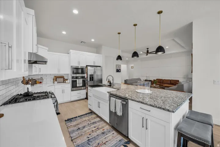 Kitchen with ceiling fan, a kitchen island with sink, white cabinets, and light stone counters
