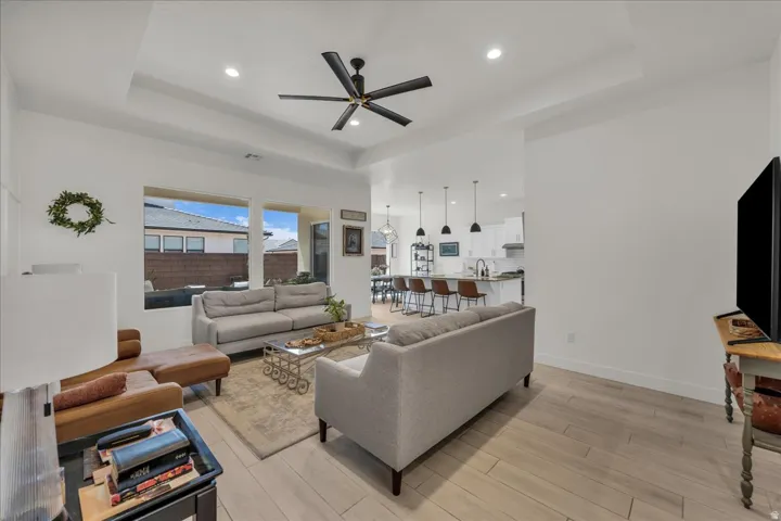 Living room with a ceiling fan, wood tiled floors, recessed lighting, and a raised ceiling