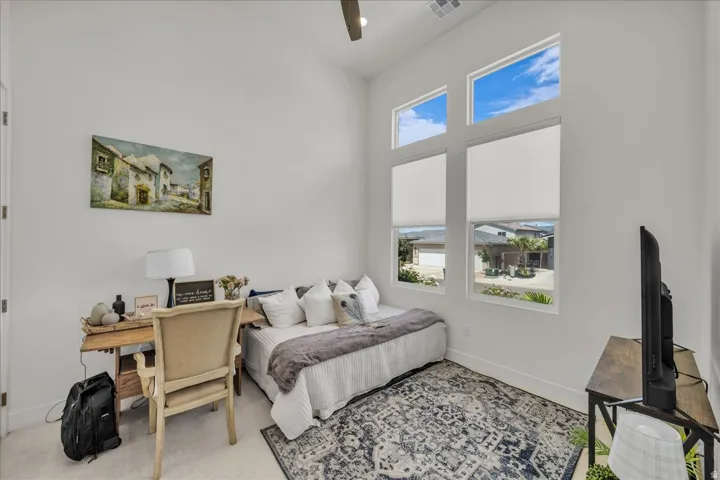 Carpeted bedroom with ceiling fan, an office area, and a high ceiling