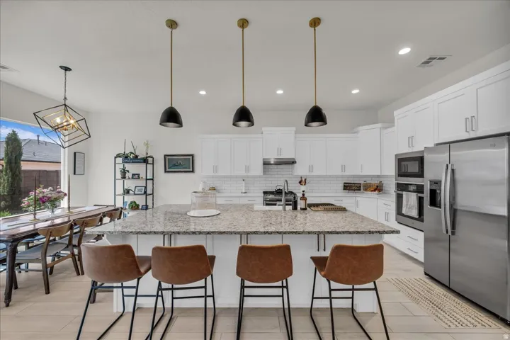 Kitchen with stainless steel appliances, light stone counters, white cabinets, and a kitchen island with sink