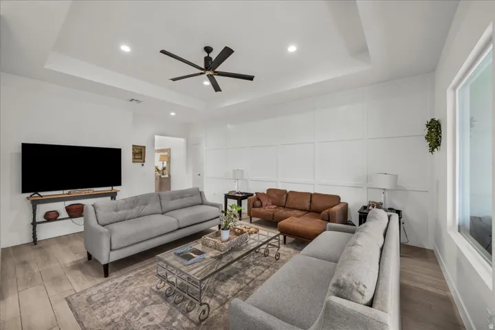 Living area with a decorative wall, wood finished floors, a ceiling fan, recessed lighting, and a raised ceiling