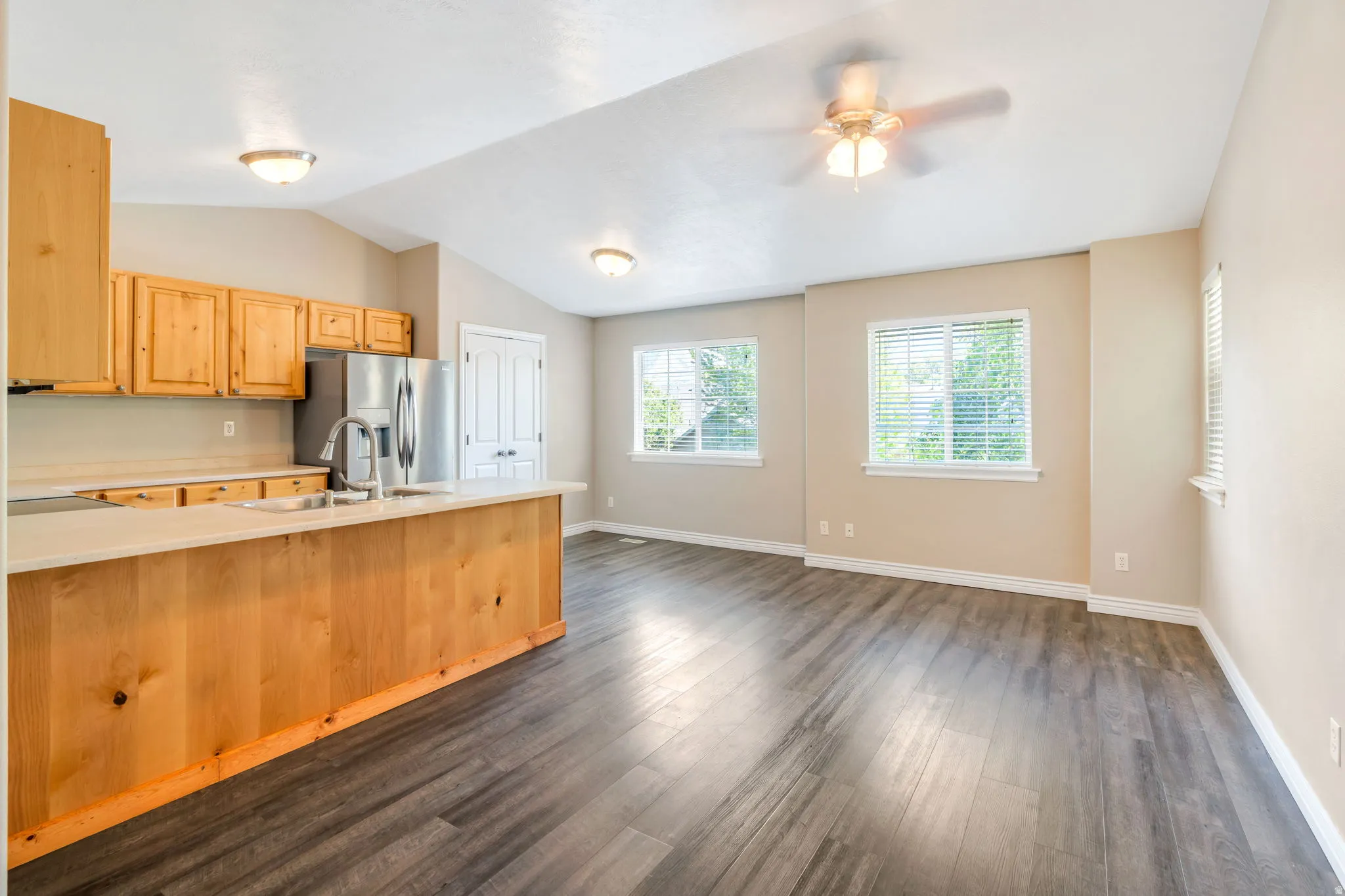 Kitchen with light wood finish cabinetry, light countertops, stainless steel refrigerator with ice dispenser, a ceiling fan, and dark wood finished floors