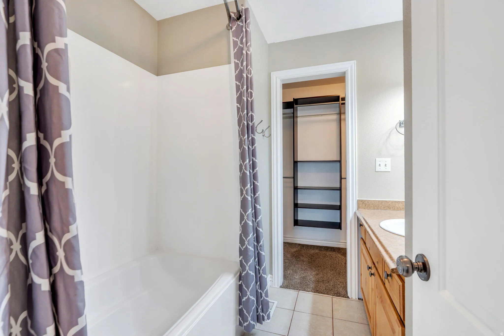 Full bath with vanity, a spacious closet, shower / bath combo with shower curtain, and light tile patterned floors