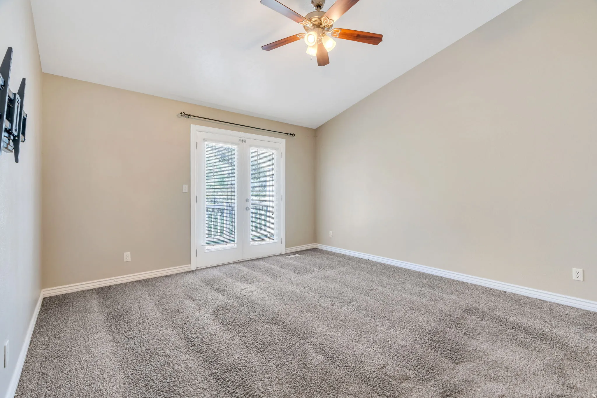 Spare room featuring light colored carpet, vaulted ceiling, french doors, and ceiling fan