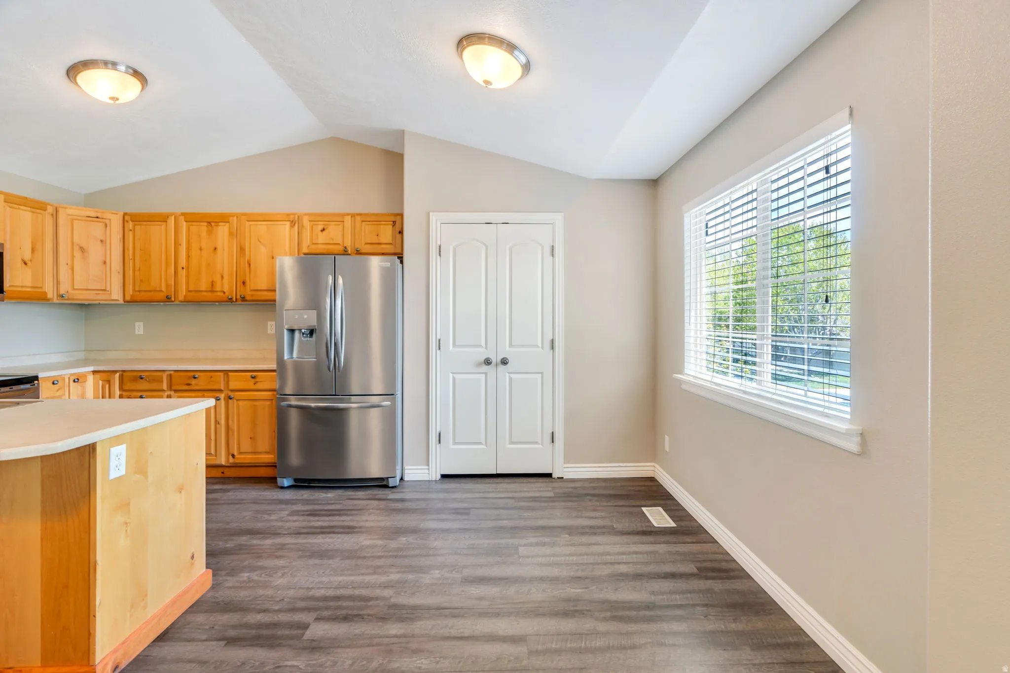 Kitchen with light countertops, stainless steel fridge with ice dispenser, dark wood-style floors, lofted ceiling, and light wood finish cabinetry