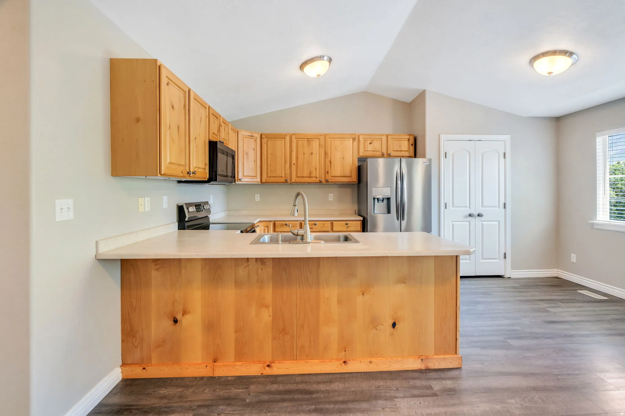 Kitchen featuring light countertops, a peninsula, stainless steel appliances, light wood finish cabinets, and dark wood-style floors