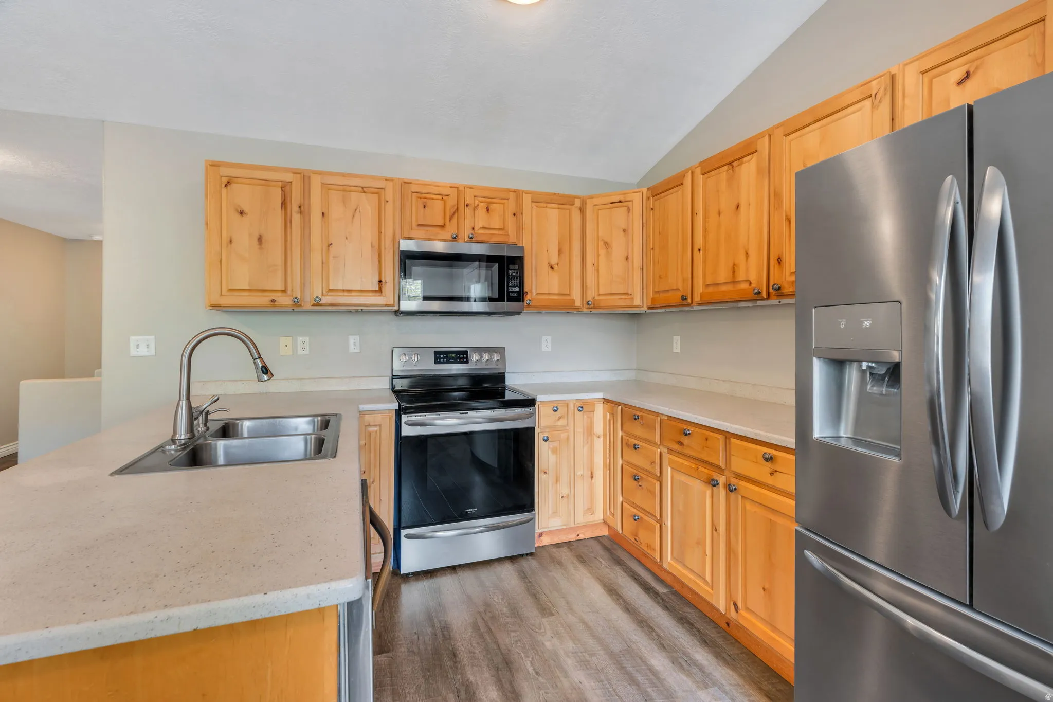 Kitchen featuring stainless steel appliances, a peninsula, lofted ceiling, dark wood-style floors, and light wood finish cabinetry