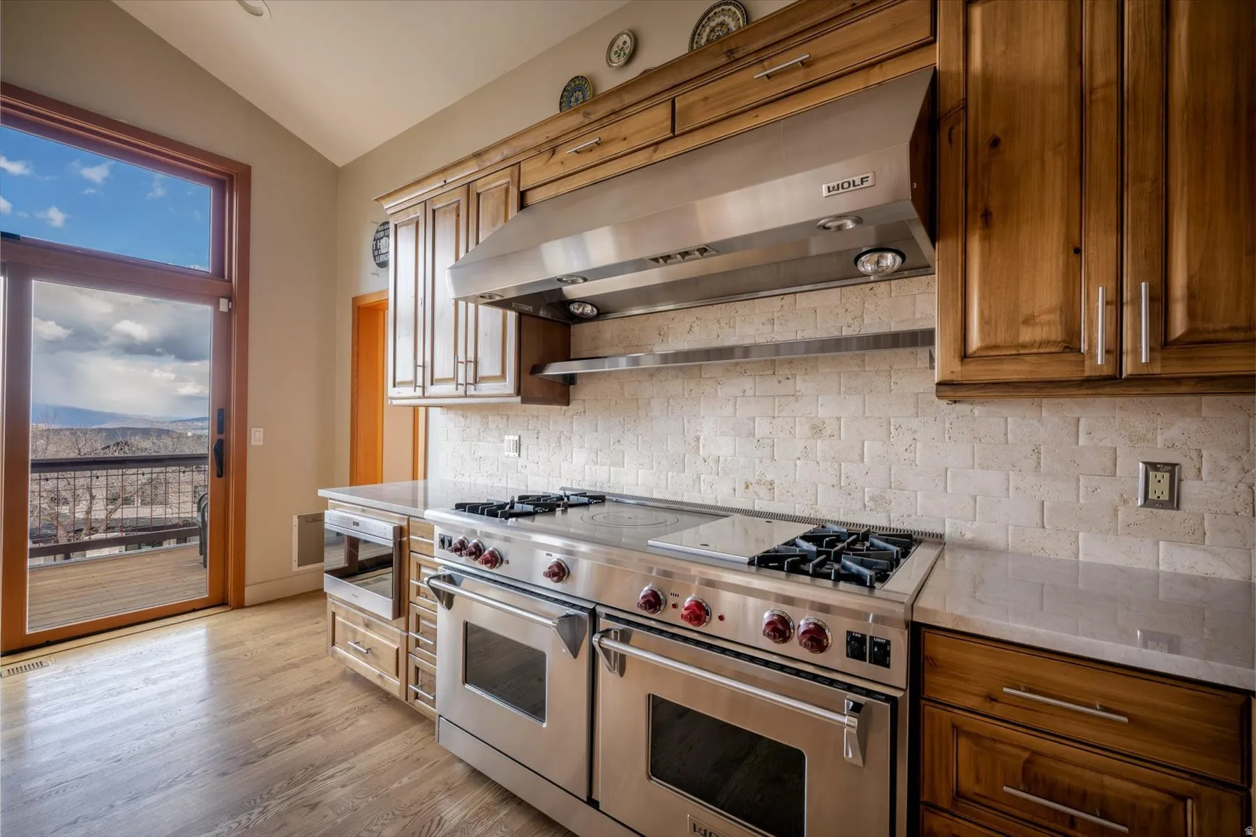 Kitchen featuring stainless steel appliances, vaulted ceiling, backsplash, and wood finish cabinetry