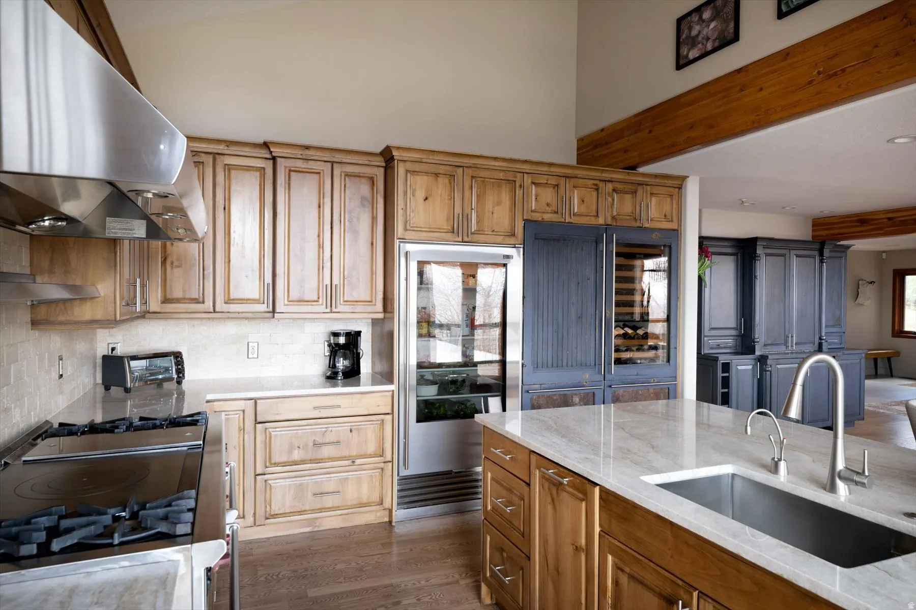 Kitchen with wood finish cabinetry, light stone countertops, tasteful backsplash, dark wood-type flooring, and gas range