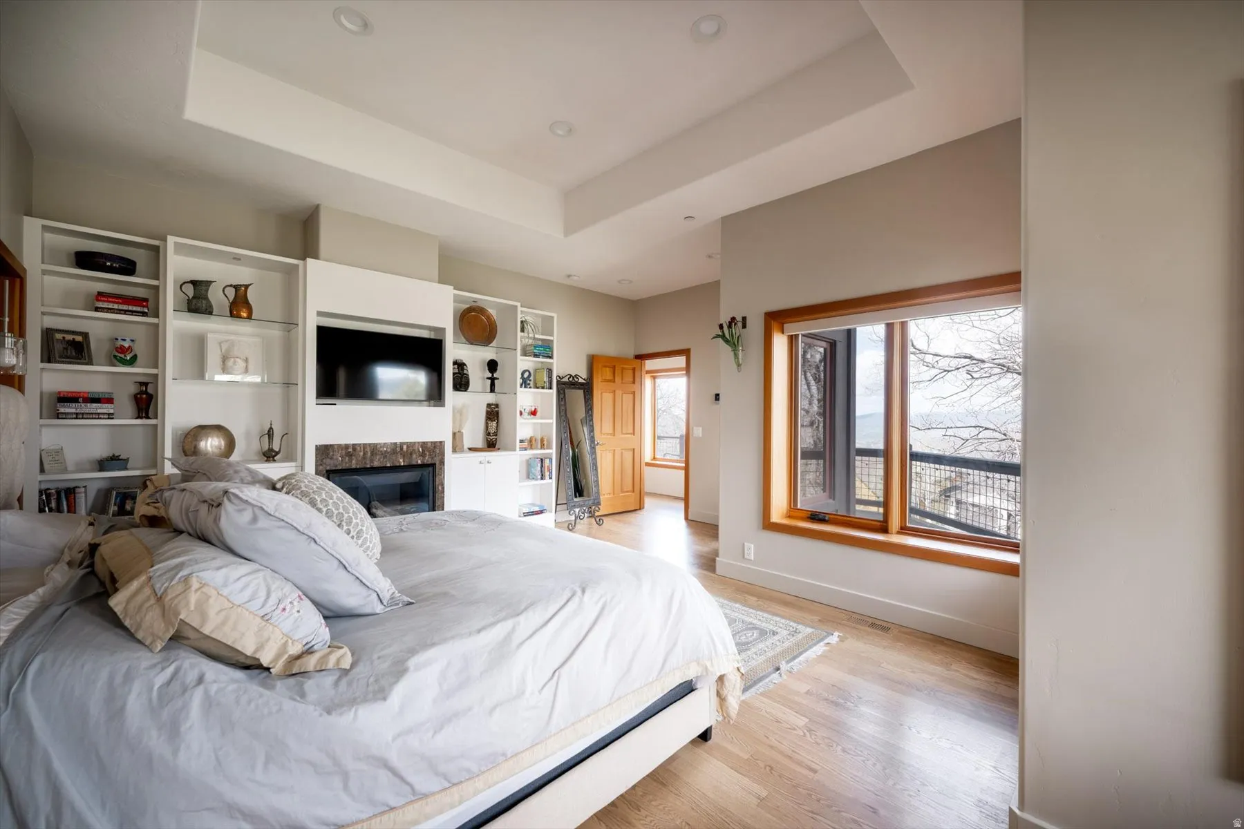 Bedroom with light wood-style floors, a raised ceiling, a premium fireplace, and recessed lighting