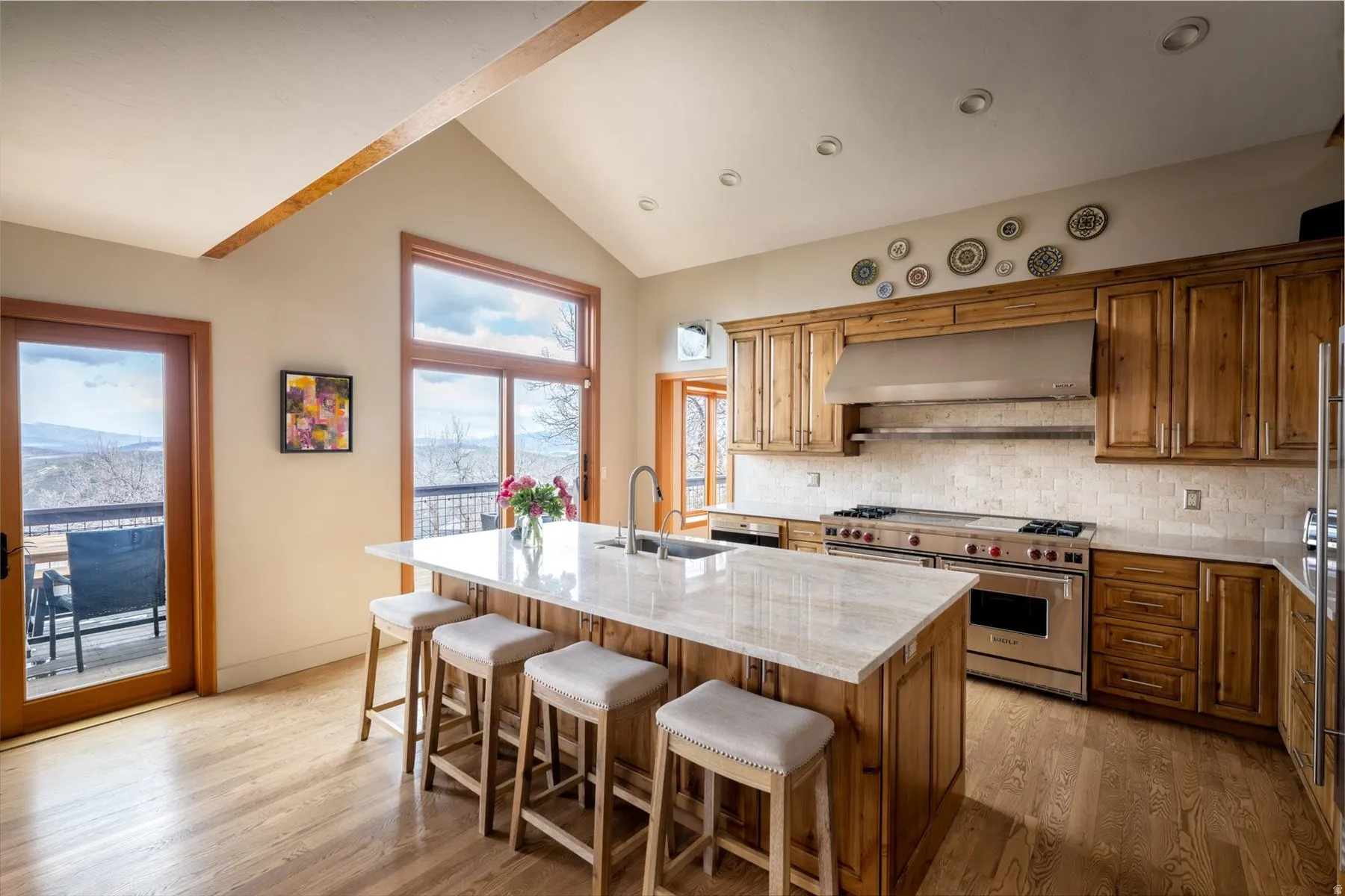 Kitchen featuring light stone counters, light wood finished floors, wood finish cabinetry, range with two ovens, and ventilation hood