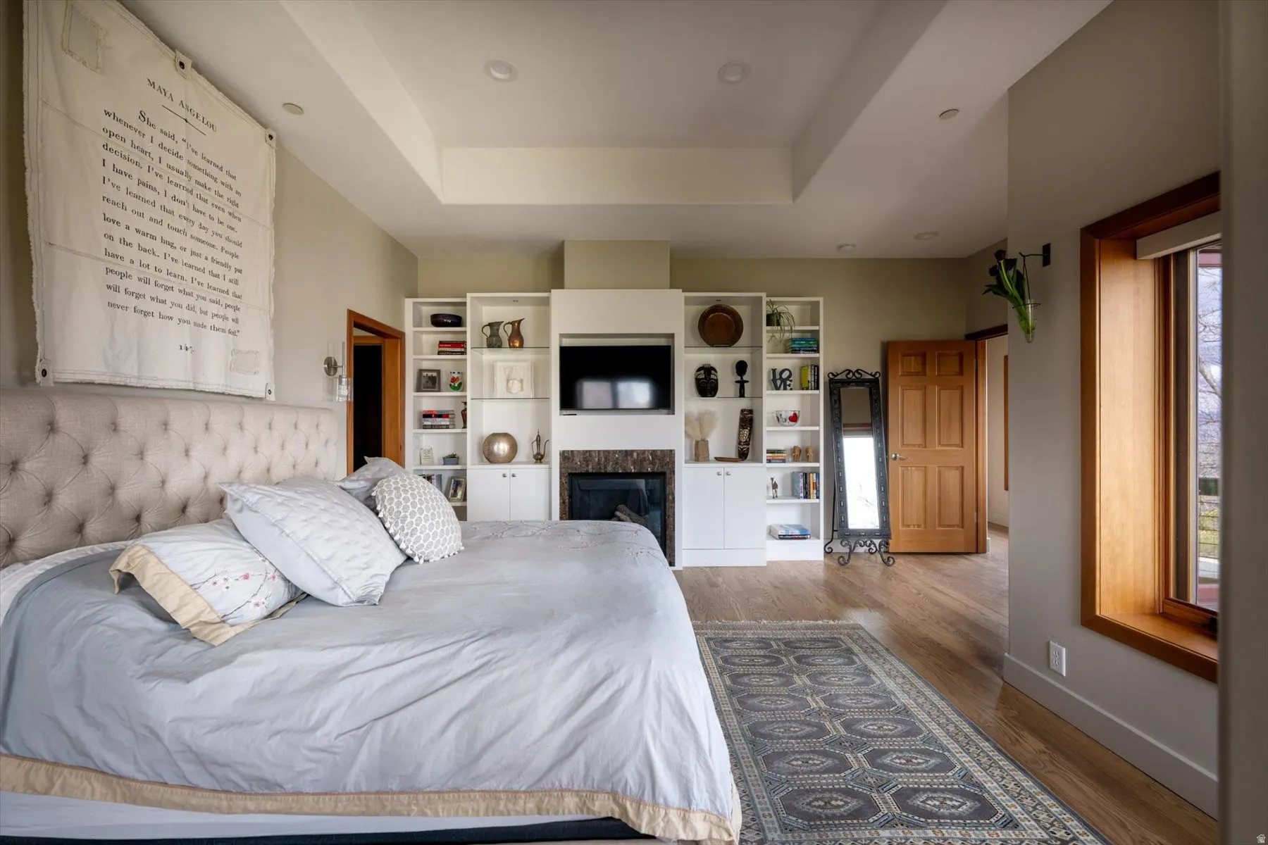 Bedroom featuring a tray ceiling, wood finished floors, and a premium fireplace