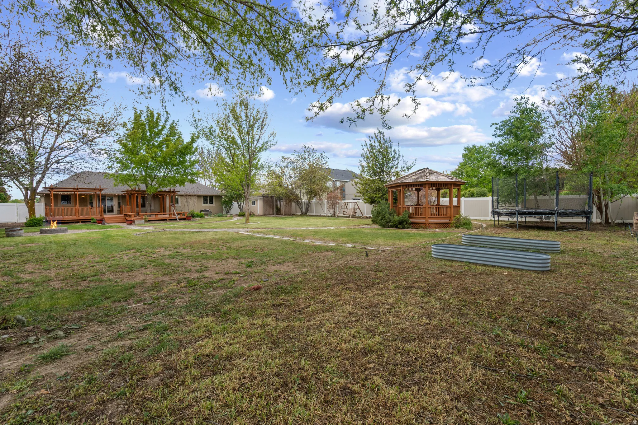 Fenced backyard featuring a trampoline and a gazebo