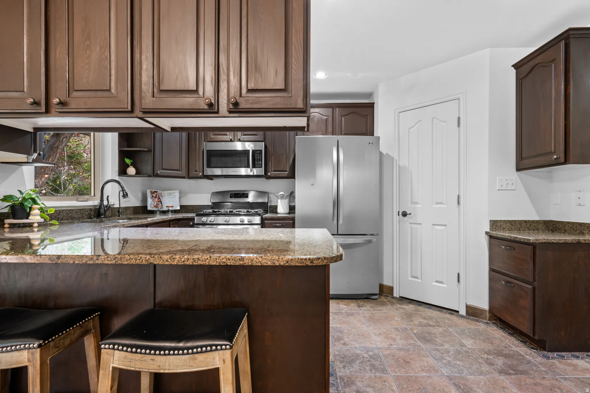 Kitchen with dark wood finish cabinets, dark stone counters, stainless steel appliances, a breakfast bar area, and a peninsula