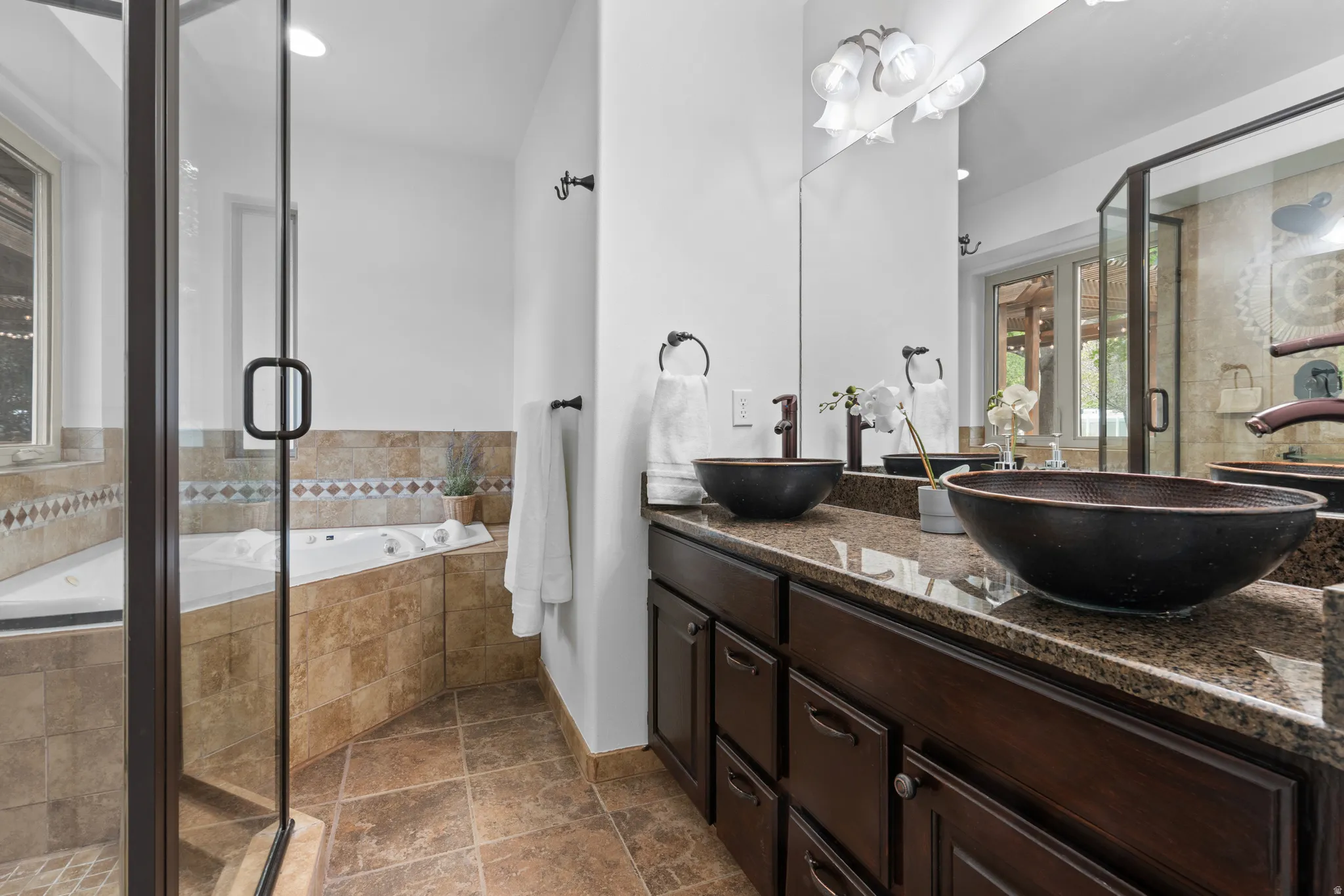 Bathroom featuring a stall shower, a garden tub, double vanity, and dark stone finish floors