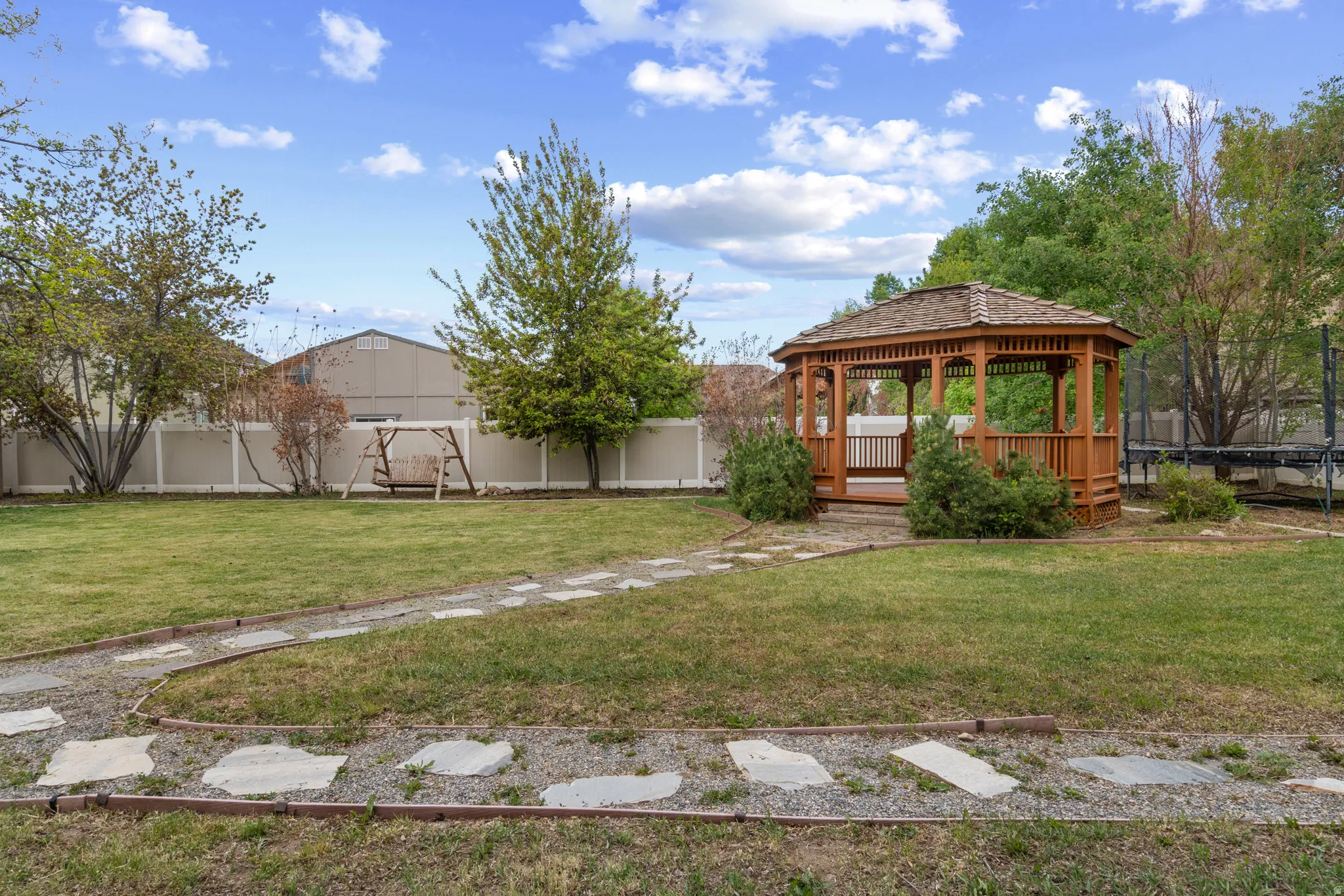 Fenced backyard featuring a gazebo, a deck, and a trampoline