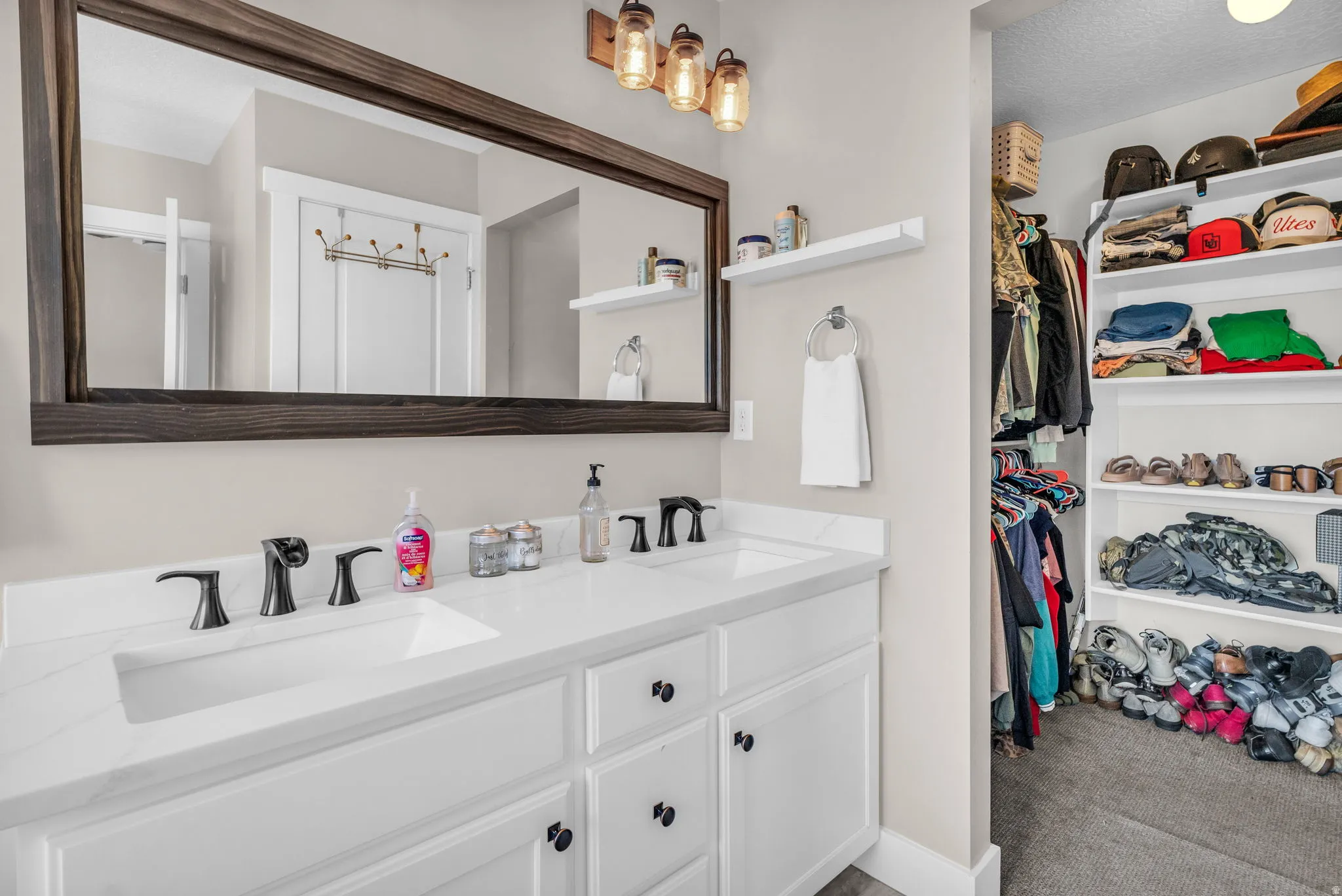 Full bath with double vanity, a spacious closet, light colored carpet, and a textured ceiling