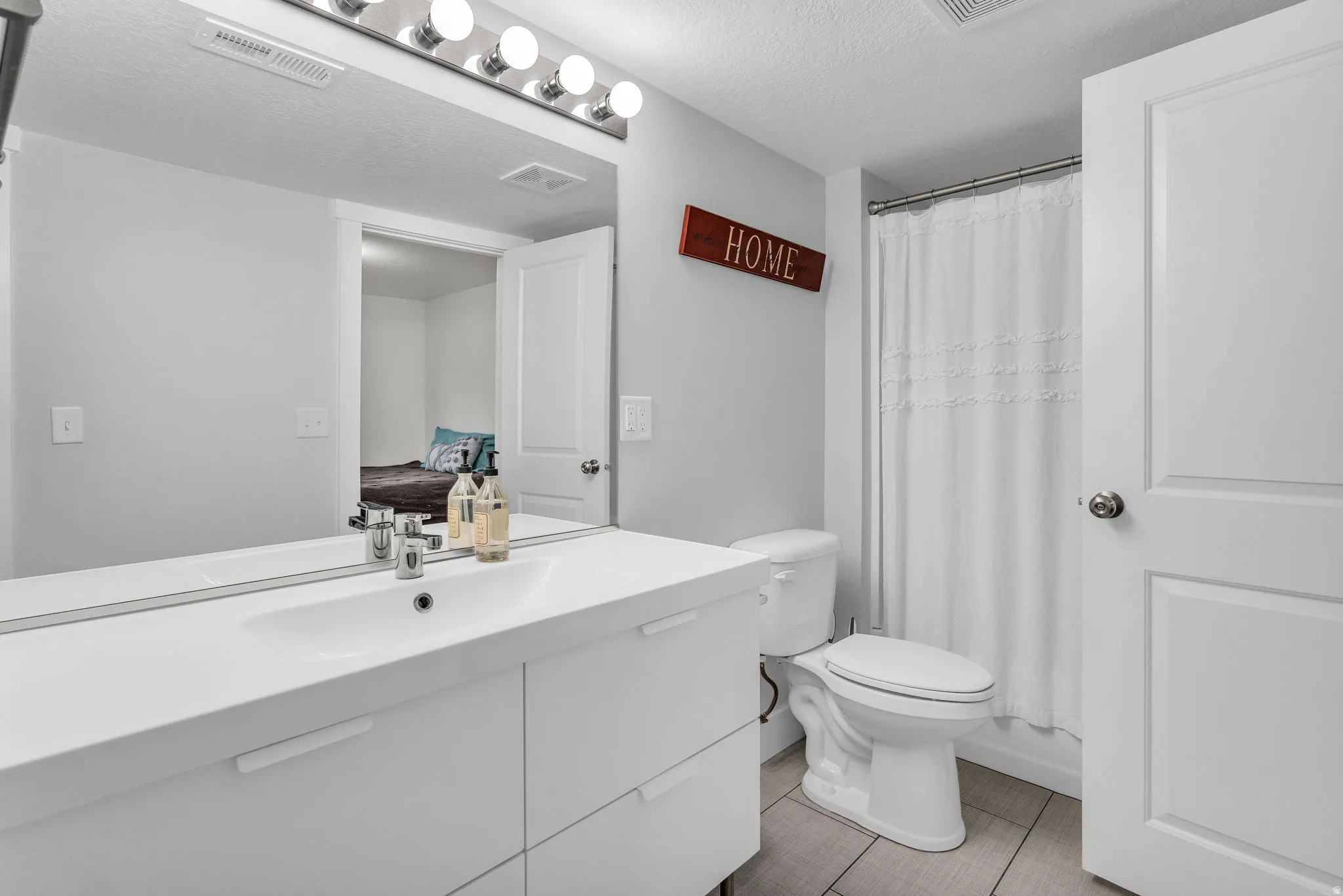 Bathroom with vanity, a textured ceiling, curtained shower, light tile patterned floors, and connected bathroom