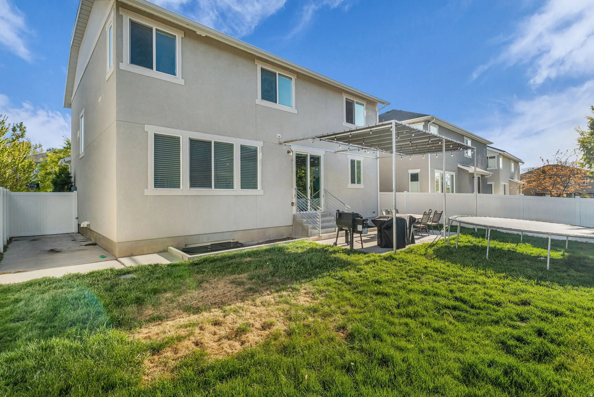 Rear view of house featuring a fenced backyard, a patio area, a trampoline, a pergola, and stucco siding