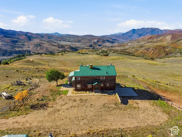 Multi-story wood siding exterior featuring a green metal roof and concrete patio, situated on a sprawling lot with mountain scenery