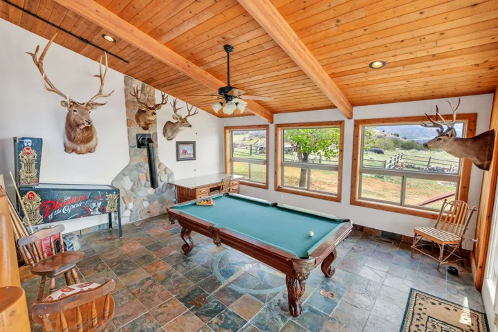 Game room with a wood stove, stone tile floors, wood ceiling, vaulted ceiling with beams, and pool table