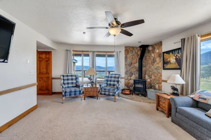Carpeted living area with a wood stove, a mountain view, a ceiling fan, a textured ceiling, and healthy amount of natural light