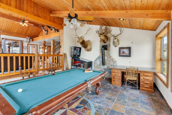 Playroom featuring dark stone finish flooring, a wood stove, wood ceiling, vaulted ceiling with beams, and ceiling fan