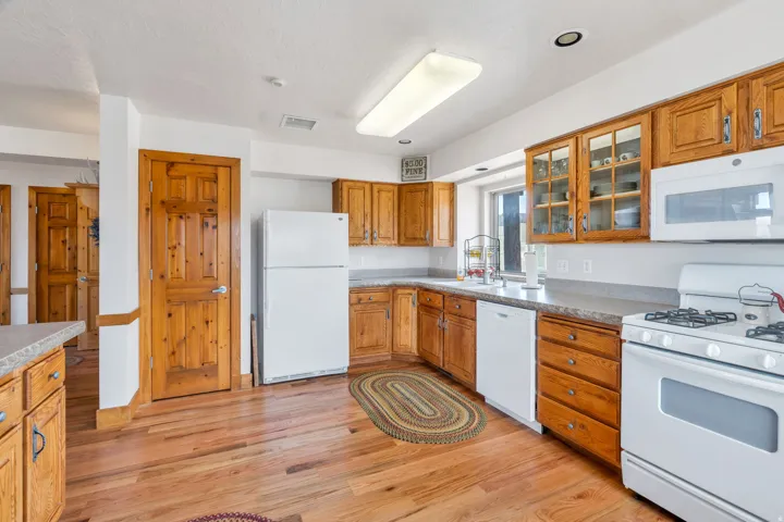 Kitchen with white appliances, light wood-style floors, glass insert cabinets, and wood finish cabinetry