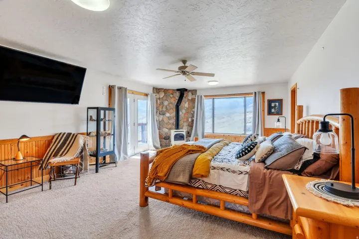 Bedroom with wooden walls, a textured ceiling, carpet flooring, a wood stove, and ceiling fan