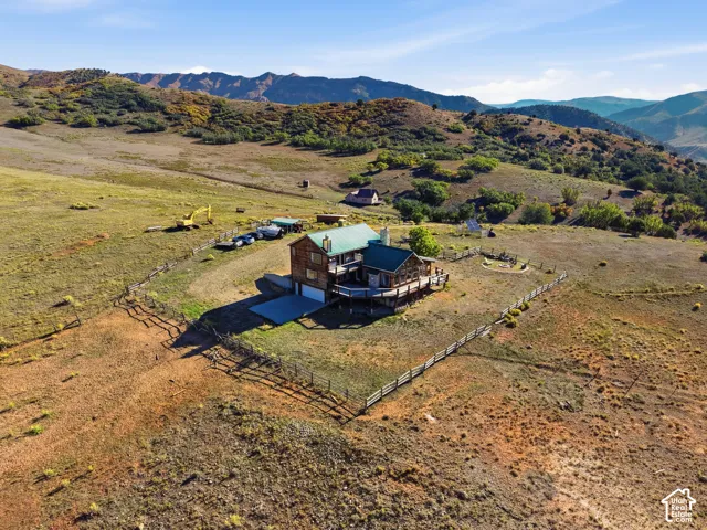 Multi-level residence with metal roofing, wrap-around decking, and concrete driveway situated on expansive acreage enclosed by perimeter fencing
