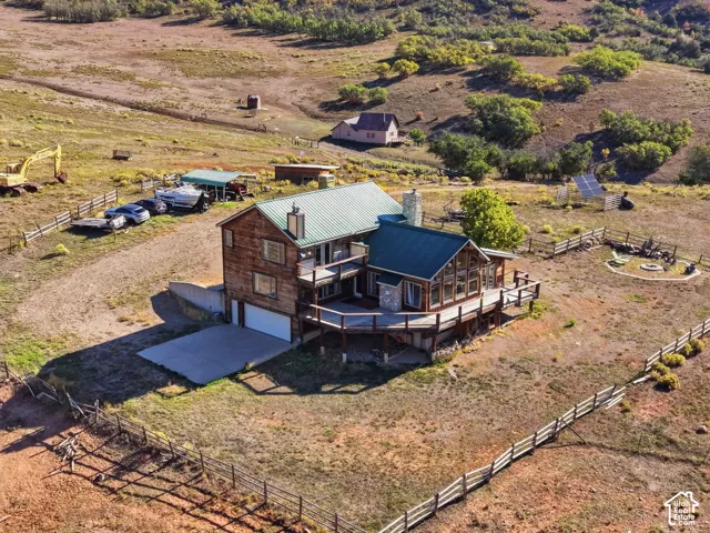 Multi-level exterior featuring wood siding, a green metal roof, a wrap-around elevated deck, and stone chimney accents situated on an expansive lot with perimeter fencing