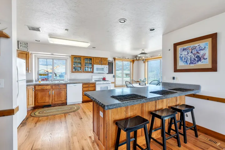 Kitchen with a breakfast bar, wood finish cabinetry, white appliances, light wood-type flooring, and glass fronted cabinets