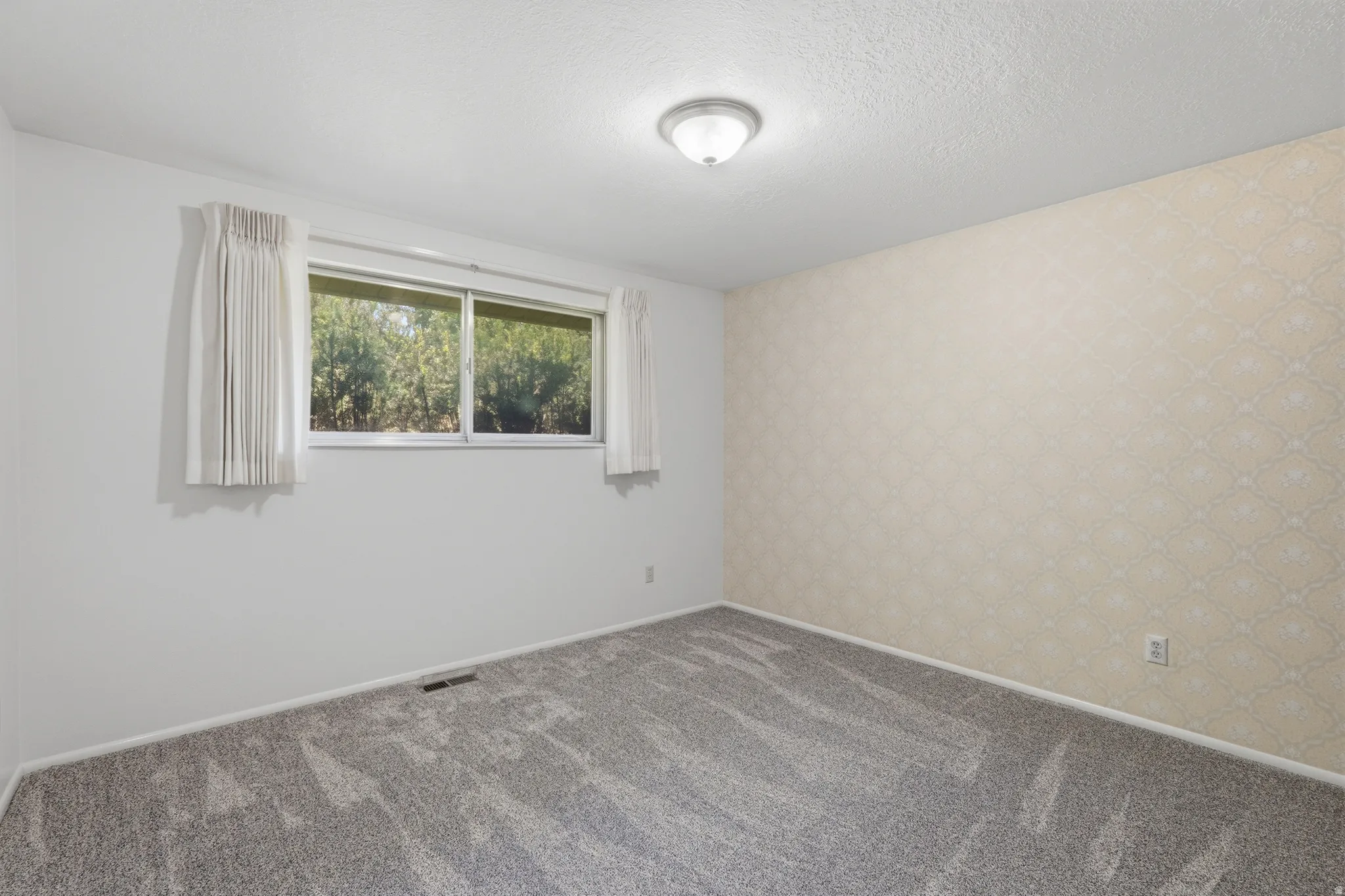 Light-filled interior space featuring a large window, neutral carpeting, and a textured accent wall
