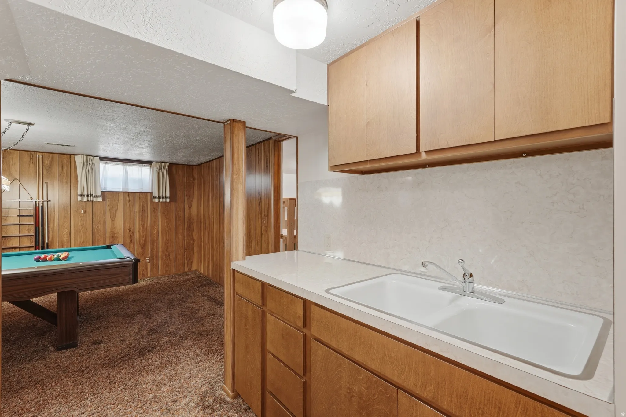 Lower level featuring a built-in wet bar with wood-finish cabinetry, a double basin sink, and a laminate countertop