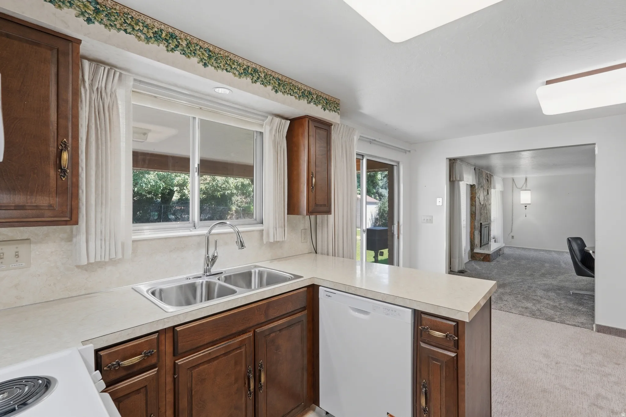 Kitchen featuring wood-finish cabinetry, a double basin stainless steel sink, and light-toned countertops