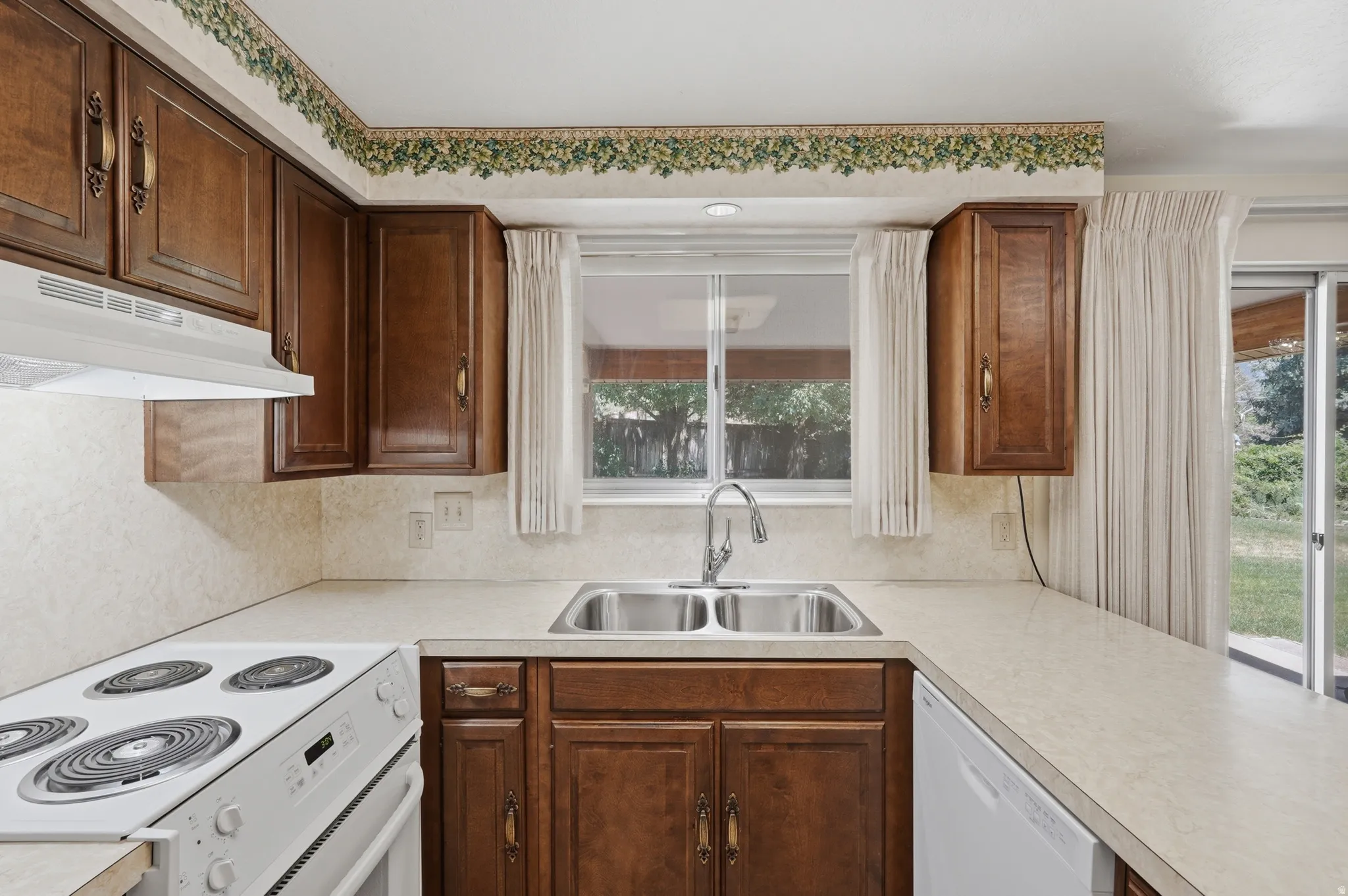 Kitchen featuring wood-finish cabinetry with decorative hardware, a double basin stainless steel sink, and a white electric range